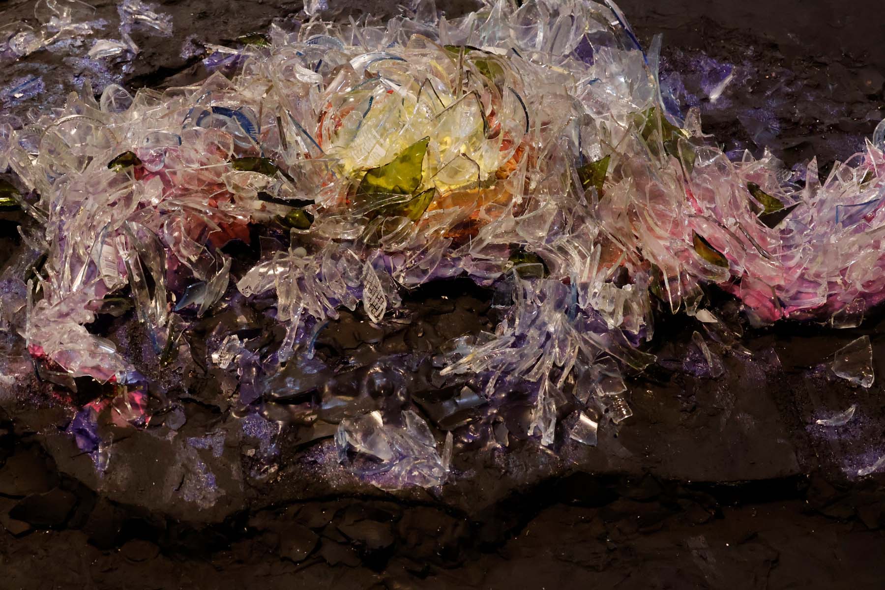 Close up of the glass layers of the sculpture. From here, printed text from some bottles is visible, as are the color differences in green and blue shards among the predominantly clear ones, and the yellows and reds from the galaxy center reflect throughout.
